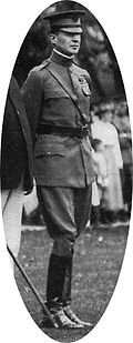 Man wearing peaked cap, Sam Browne belt, and shiny riding boots.
