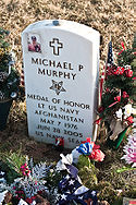 A military grave stone with an image of a man with a cross next to it. Also shows the name of the indivual and info about them with an image of the Medal of Honor.