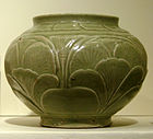 A green-grey bowl with a small bottom, a very wide center, and a top opening wider than the base but not as wide as the center. A pattern of out-dented large leaves covers the body of the bowl.