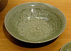A grey-green shallow bowl or curved plate with a large orchid design painted into the inside of the bowl.