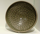 A grey-green shallow bowl with a painted decoration on the inside consisting of dozens of small petals moving outward from the center of the dish in a spiral pattern.