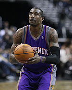 A man, wearing a purple jersey with a word "PHOENIX" written in the front, is holding a basketball.
