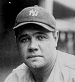 A man in a baseball cap reading "NY" looks into the camera. The picture shows only his head and shoulders. The man has large eyebrows, a wide nose, and a cleft in his chin.