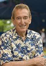 A man in a Hawaiian floral shirt looks directly at the viewer.