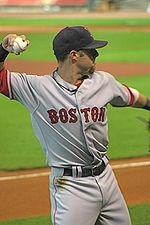 A man in a gray baseball uniform with "BOSTON" across the chest and a dark cap prepares to throw with his right arm.