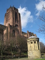 Small circular stone building, with a large brick cathedral building immediately behind it
