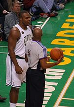 A basketball player stands on a basketball court. He wears a green jersey with the word "CELTICS" and the number 11 on the front.