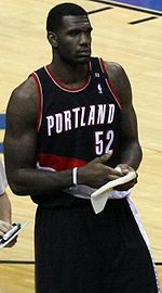 A basketball player, wearing a black jersey with the word "PORTLAND" and the number 52 on the front, stands on a basketball court.