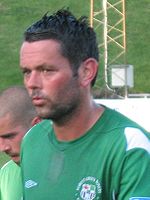 Head and shoulders of dark-haired white man wearing a green sports shirt