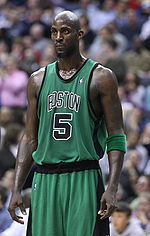 A man, wearing a green jersey with a word "BOSTON" and the number "5" written in the front, is standing in front of the crowd.