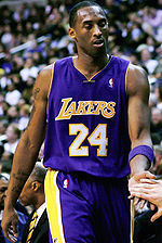 A man, wearing a purple jersey with a word "LAKERS" and the number "24" written in the front, is standing in front of the crowd.