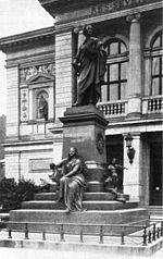 black and white photograph of a statue of a robed male figure on a stepped pedestal, inscribed 'Felix Mendlessohn Bartholdy', with a seated female figure holding a lyre at its base, in front of an arcaded building
