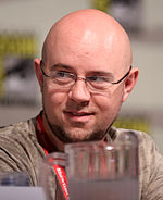 A black and white photograph of a man with a small beard and a bald head, wearing glasses.