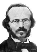 The head of a man with a large forehead and receding hair, a mustache and soul patch, and long thick sideburns, wearing small wire-rimmed glasses and a dark bow-tie