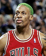 A black man with green-dyed hair, wearing a red basketball jersey with the word "BULLS" in the front, looks into the camera