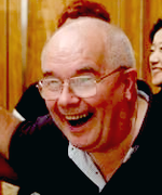 a bespectacled man with thin grey hair, laughing
