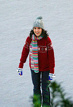 Smiling, dark-haired woman wearing winter clothes, standing in a snowy field.