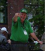 A man wearing a green t-shirt and a green cap with a word "CELTICS" are pointing his hand towards the camera.