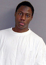 A young African man with dark skin, short black hair, and brown eyes, wearing a white T-shirt.