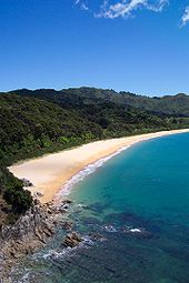 Photo showing clear blue water, a golden sanded beach and forested hills