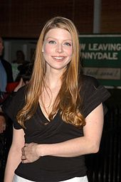 Amber Benson stands, smiling, with her left forearm over her waist.  Behind her is a green banner that reads "Now leaving Sunnydale. Come back soon."
