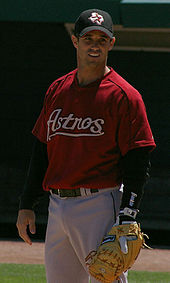 A baseball player standing at first base with his glove, wearing a red jersey with the word "Astros" in front