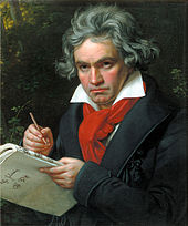 A man with long grey hair holding a pen and music paper