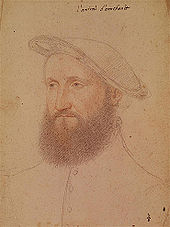 A middle-aged man with a full, curly beard wearing a high-collared jacket and a flat beret-like hat slanting to the left side of his head