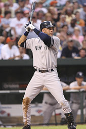 A man in a grey baseball uniform with "New York" written on the front in navy letters and a navy helmet stands in a batting stance while holding a baseball bat.