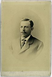 A man in a suit shown from the chest up is facing slightly right of the camera.