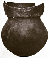  A ceramic pot with a round bottom, short neck, and a rim decorated with geometric line patterns. The rim is broken in the rear.
