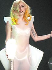A blond female, holding a lighted-bulb stick. She has yellow curls and wears a translucent white dress.