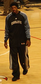 A black person wearing a black team jacket and pants walking on a basketball court