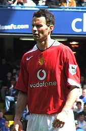 A photograph of a man with dark hair and a focused expression on his face, wearing a red shirt and white shorts.
