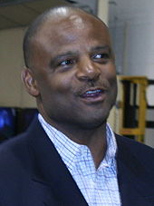 Head and shoulders of a bald black man wearing a light shirt and a black suit jacket.