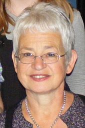 A portrait of a bespectacled, smiling middle-aged woman with short, light grey hair.