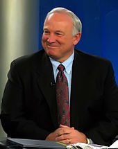 Waist high portrait of man in his sixties, smiling in a black suit