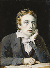 Miniature of Keats in his twenties, a pale sensitive young man with large blue eyes looking up from a book on the table in front of him, with his chin on his left hand with his elbow. He has tousled golden-brown hair parted in the middle, and wears a grey jacket and waistcoat over a shirt with a soft collar and white cravate tied in a loose bow.