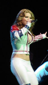 A woman is performing a song over the stage. She wears a white jacket and pants.