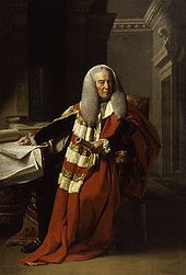 A full-length portrait of an elderly man, seated.  He wears long flowing red and white robes, a long grey wig, and holds a rolled document in his left hand.  His right hand rests on a table littered with documents.  Behind him, the corner of a room, with ornate plaster architrave, is visible.