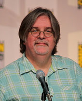 A man in glasses and a plaid shirt sits in front of a microphone.