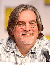  A man in glasses and a plaid shirt sits in front of a microphone.
