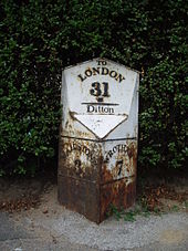 A photograph showing a small monument at the roadside. The bottom of the white cast-iron monument is v-shaped towards the road. The right hand side reads 'WROTHAM 7' and the left reads 'MAIDSTONE 3'. There is rust damage to its base. On the head of the monument, parallel to the road, the legend, in black-painted relief, reads 'To LONDON 31'