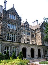 A four-story Gothic building with three entrance archways and historic balconies with evergreen trees at base and stairwells leading to each entrance