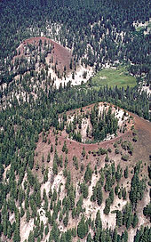Two red cinder cones in a forest. There is a meadow at the base of one of the ones