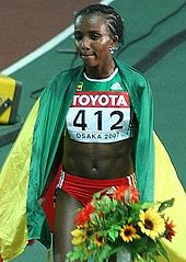 Tirunesh Dibaba in a green running vest covered in a flag, holding a bouquet of flowers