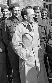 Tommy Douglas stands in front of a group of men in military uniform.