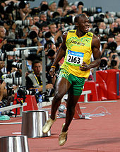 Black athlete Usain Bolt in a yellow running vest and green shorts just completing a race