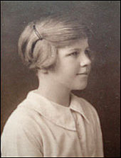Head-and-shoulders photograph of a young girl. She wears a light-coloured blouse and faces right, looking out of the picture, with a slight smile. Her short hair is pulled back from her face and pinned up.