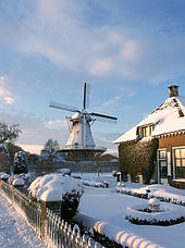 Snow in front of Dutch house, with windmill in background